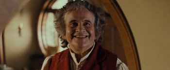 Movie still from “The Lord of the Rings: The Fellowship of the Ring” (2001), directed by Peter Jackson – An older man with curly grey hair smiling for the camera; Close Up shot, Low angle