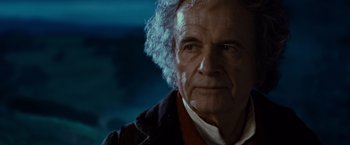 Movie still from “The Lord of the Rings: The Fellowship of the Ring” (2001), directed by Peter Jackson – An older man with white curly hair wearing a jacket; Close Up shot, Over the shoulder angle