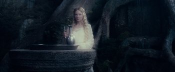 Movie still from “The Lord of the Rings: The Fellowship of the Ring” (2001), directed by Peter Jackson – A woman in a white dress standing in front of a fountain; Medium shot, Low angle