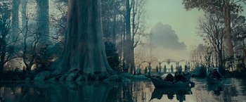 Movie still from “The Lord of the Rings: The Fellowship of the Ring” (2001), directed by Peter Jackson – A group of people standing around a body of water near trees; Extreme Wide shot, High angle