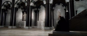 Movie still from “The Lord of the Rings: The Return of the King” (2003), directed by Peter Jackson – A person sitting on a bench in front of a statue; Wide shot, High angle