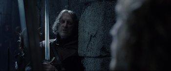 Movie still from “The Lord of the Rings: The Return of the King” (2003), directed by Peter Jackson – A man with long white hair is standing next to a stone wall; Close Up shot, Over the shoulder angle