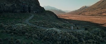 Movie still from “The Lord of the Rings: The Two Towers” (2002), directed by Peter Jackson – A person standing on a dirt road near a mountain; Extreme Wide shot, High angle