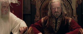 Movie still from “The Lord of the Rings: The Two Towers” (2002), directed by Peter Jackson – An older man sitting in a chair wearing a red and brown shirt; Medium shot, Over the shoulder angle
