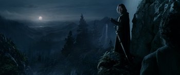 Movie still from “The Lord of the Rings: The Two Towers” (2002), directed by Peter Jackson – A man standing on top of a hill with a sword; Wide shot, Low angle