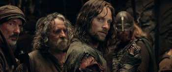 Movie still from “The Lord of the Rings: The Two Towers” (2002), directed by Peter Jackson – A man with long hair is standing next to another man with long hair; Close Up shot, Over the shoulder angle