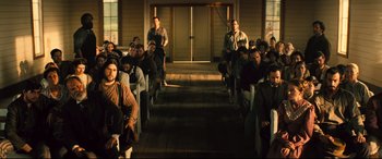 Movie still from “The Magnificent Seven” (2016), directed by Antoine Fuqua – A group of people sitting in front of a building; Wide shot, High angle