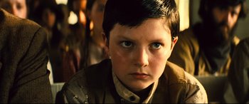 Movie still from “The Magnificent Seven” (2016), directed by Antoine Fuqua – A young boy is looking into the camera; Close Up shot, Low angle