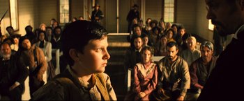 Movie still from “The Magnificent Seven” (2016), directed by Antoine Fuqua – A group of people sitting in front of each other; Medium shot, Over the shoulder angle