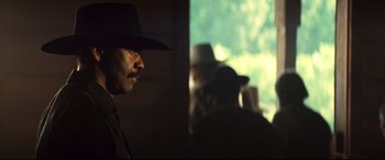 Movie still from “The Magnificent Seven” (2016), directed by Antoine Fuqua – A man wearing a cowboy hat in front of a window; Close Up shot, Over the shoulder angle