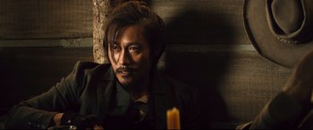 Movie still from “The Magnificent Seven” (2016), directed by Antoine Fuqua – A man sitting in front of a wall with a lit candle; Close Up shot, Over the shoulder angle