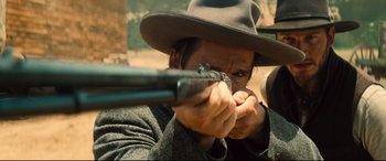 Movie still from “The Magnificent Seven” (2016), directed by Antoine Fuqua – A man with a hat is holding a gun; Close Up shot, Over the shoulder angle