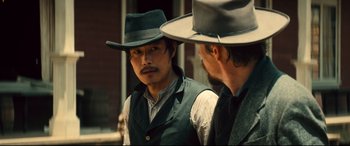 Movie still from “The Magnificent Seven” (2016), directed by Antoine Fuqua – A man in a cowboy hat and a man with a beard; Medium shot, Over the shoulder angle