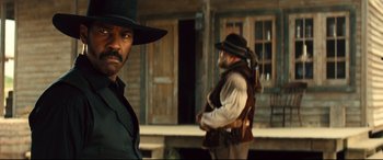 Movie still from “The Magnificent Seven” (2016), directed by Antoine Fuqua – A man in a cowboy hat standing next to another man in a cowboy hat; Medium shot, Over the shoulder angle