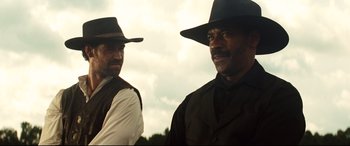 Movie still from “The Magnificent Seven” (2016), directed by Antoine Fuqua – A couple of men standing next to each other wearing hats; Medium shot, Low angle