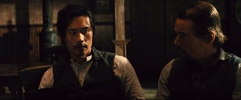 Movie still from “The Magnificent Seven” (2016), directed by Antoine Fuqua – A man with a mustache sitting next to another man; Close Up shot, Over the shoulder angle