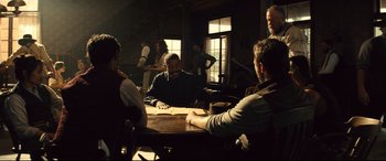 Movie still from “The Magnificent Seven” (2016), directed by Antoine Fuqua – A group of people sitting around a table; Wide shot, Over the shoulder angle