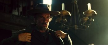 Movie still from “The Magnificent Seven” (2016), directed by Antoine Fuqua – A man with a beard and a hat is standing in a dimly - lit room; Close Up shot, Over the shoulder angle