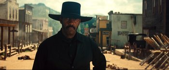 Movie still from “The Magnificent Seven” (2016), directed by Antoine Fuqua – A man in a black hat standing in front of buildings; Medium shot, Low angle