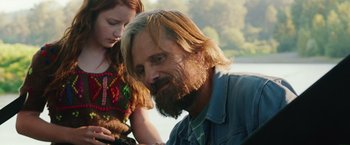 A man with long hair and a long beard is sitting next to a little girl