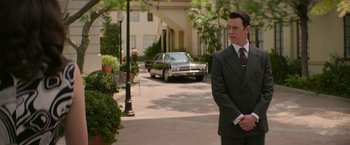 Movie still from “The Offer” (2022), directed by Dexter Fletcher – A man in a suit and tie standing in front of a car on the street; Medium shot, Over the shoulder angle