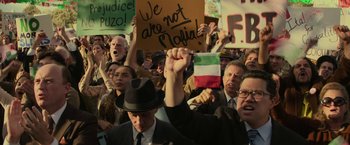 Movie still from “The Offer” (2022), directed by Dexter Fletcher – A group of people holding up signs in front of a crowd of onlookers; Medium shot, High angle