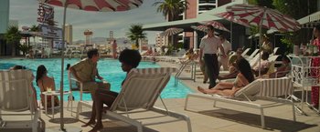 Movie still from “The Offer” (2022), directed by Dexter Fletcher – A group of people sitting on lounge chairs next to a swimming pool; Extreme Wide shot, High angle