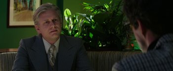 Movie still from “The Offer” (2022), directed by Dexter Fletcher – A man in a suit sitting in front of some plants; Close Up shot, Over the shoulder angle