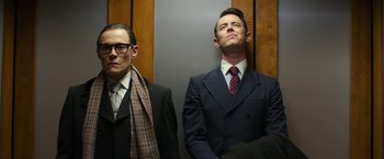Movie still from “The Offer” (2022), directed by Dexter Fletcher – A man in a suit and tie next to another man in a suit and tie in an elevator; Medium shot, Low angle