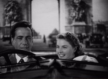 Movie still from “Casablanca” (1942), directed by Michael Curtiz – A black and white photo of a man and a woman in the backseat of a car; Medium shot, High angle