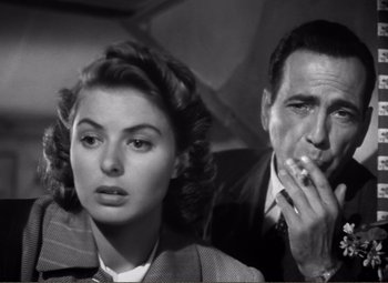 Movie still from “Casablanca” (1942), directed by Michael Curtiz – A man and a woman sitting next to each other in front of an umbrella; Close Up shot, Low angle