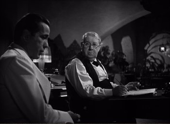 Movie still from “Casablanca” (1942), directed by Michael Curtiz – A man sitting at a table with another man in front of him; Medium shot, Over the shoulder angle
