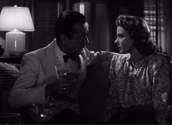 Movie still from “Casablanca” (1942), directed by Michael Curtiz – A man and a woman sitting next to each other holding wine glasses; Medium shot, Over the shoulder angle
