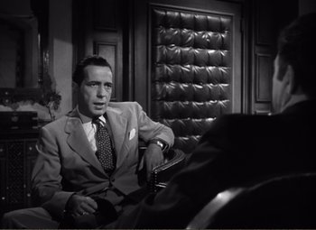 Movie still from “Casablanca” (1942), directed by Michael Curtiz – A man in a suit and tie sitting in a chair; Medium shot, Over the shoulder angle