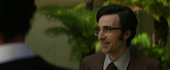 Movie still from “The Offer” (2022), directed by Dexter Fletcher – A person wearing glasses and a suit; Close Up shot, Over the shoulder angle