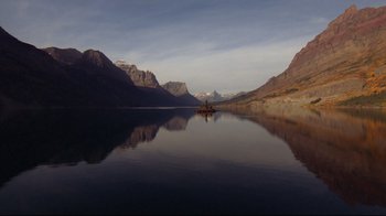 Movie still from “The Shining” (1980), directed by Stanley Kubrick – A boat floating on top of a body of water near mountains; Extreme Wide shot, High angle