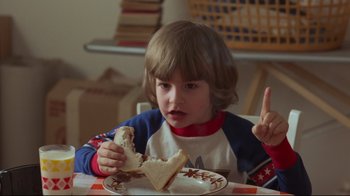 Movie still from “The Shining” (1980), directed by Stanley Kubrick – A young boy sitting at a table eating a sandwich; Medium shot, High angle