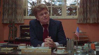 Movie still from “The Shining” (1980), directed by Stanley Kubrick – A man sitting at a table in front of an american flag; Medium shot, Over the shoulder angle