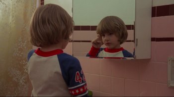 Movie still from “The Shining” (1980), directed by Stanley Kubrick – A young boy looking at himself in the mirror; Close Up shot, Over the shoulder angle