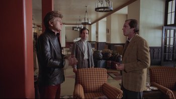 Movie still from “The Shining” (1980), directed by Stanley Kubrick – A group of men standing in a living room talking; Wide shot, Over the shoulder angle