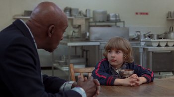 Movie still from “The Shining” (1980), directed by Stanley Kubrick – A young boy sitting at a table with an older man; Medium shot, Over the shoulder angle