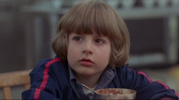 Movie still from “The Shining” (1980), directed by Stanley Kubrick – A young boy is holding a bowl of cereal; Close Up shot, Over the shoulder angle