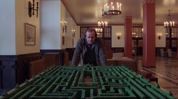 Movie still from “The Shining” (1980), directed by Stanley Kubrick – A man standing in front of a large green maze; Wide shot, High angle