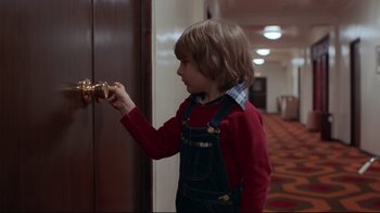 Movie still from “The Shining” (1980), directed by Stanley Kubrick – A young boy is opening the door of a hotel room; Medium shot, Over the shoulder angle