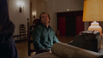 Movie still from “The Shining” (1980), directed by Stanley Kubrick – A man sitting in a chair in front of a couch; Medium shot, Low angle