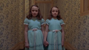 Movie still from “The Shining” (1980), directed by Stanley Kubrick – Two identical twin girls in blue dresses holding hands in front of a mirror; Medium shot, Low angle