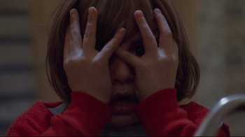 Movie still from “The Shining” (1980), directed by Stanley Kubrick – A young child covering his eyes with their hands; Close Up shot, High angle