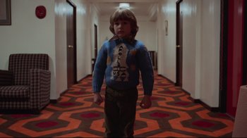 Movie still from “The Shining” (1980), directed by Stanley Kubrick – A young boy wearing a sweater in the hallway of a hotel; Medium shot, Low angle