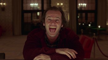 Movie still from “The Shining” (1980), directed by Stanley Kubrick – A man with long hair and a red shirt is laughing; Medium shot, Low angle