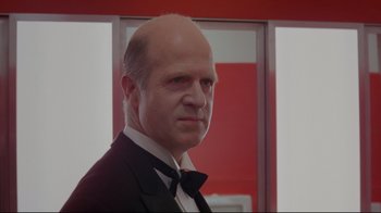 Movie still from “The Shining” (1980), directed by Stanley Kubrick – A bald man in a suit and bow tie in front of a red wall; Close Up shot, Low angle